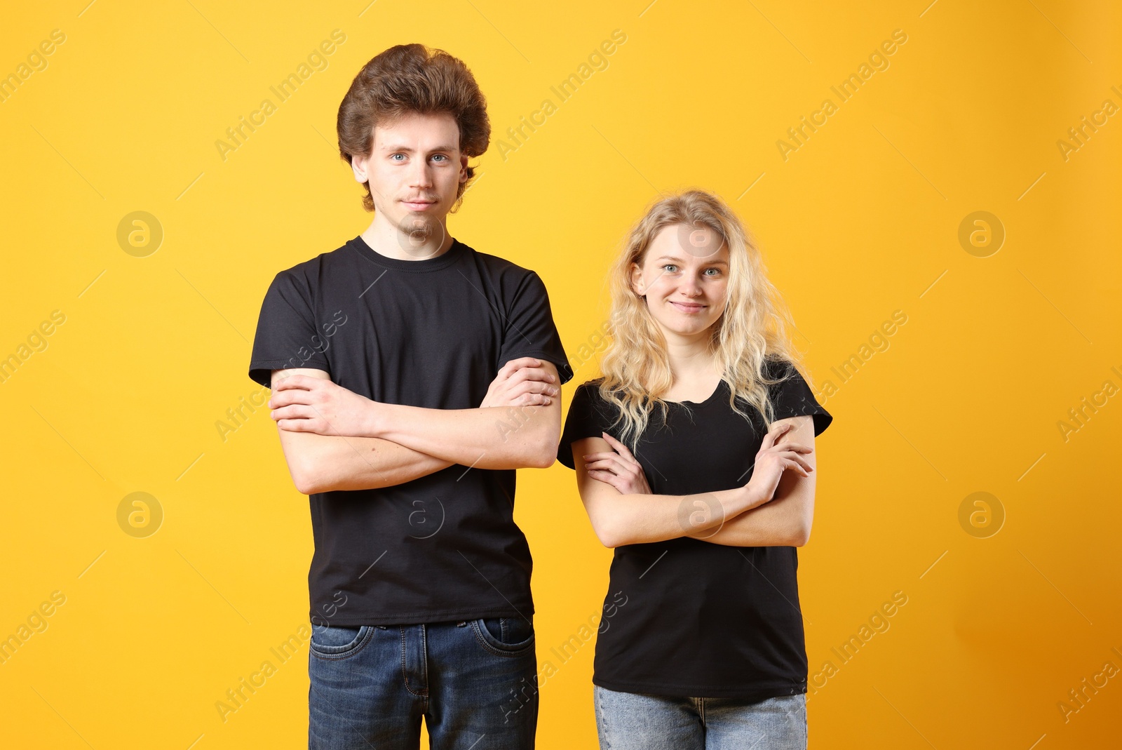 Photo of Young woman and man wearing blank black t-shirts on orange background. Mockup for design