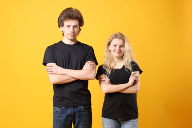 Photo of Young woman and man wearing blank black t-shirts on orange background. Mockup for design