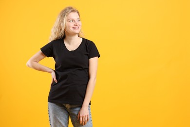 Photo of Young woman wearing blank black t-shirt on orange background. Mockup for design