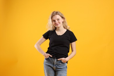 Photo of Young woman wearing blank black t-shirt on orange background. Mockup for design