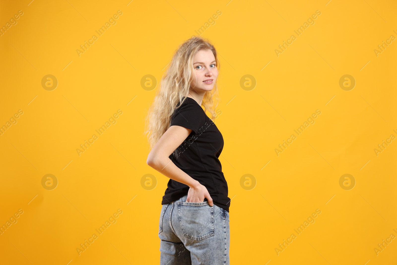 Photo of Young woman wearing blank black t-shirt on orange background. Mockup for design