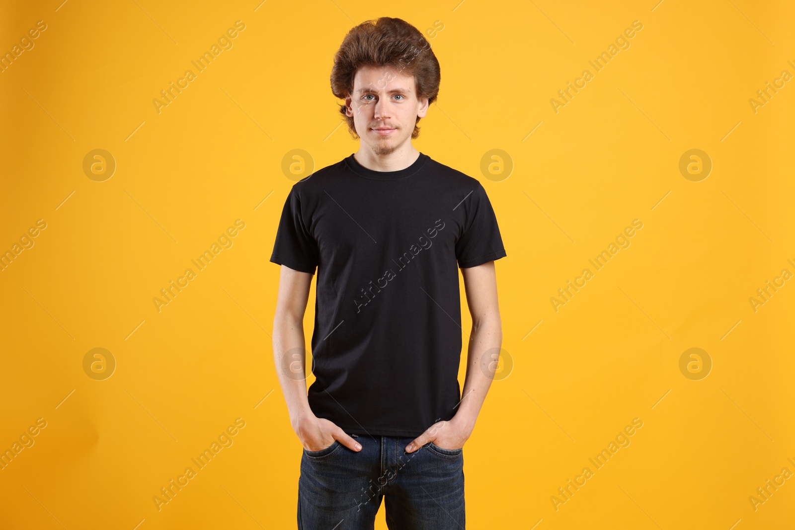 Photo of Young man wearing blank black t-shirt on orange background. Mockup for design