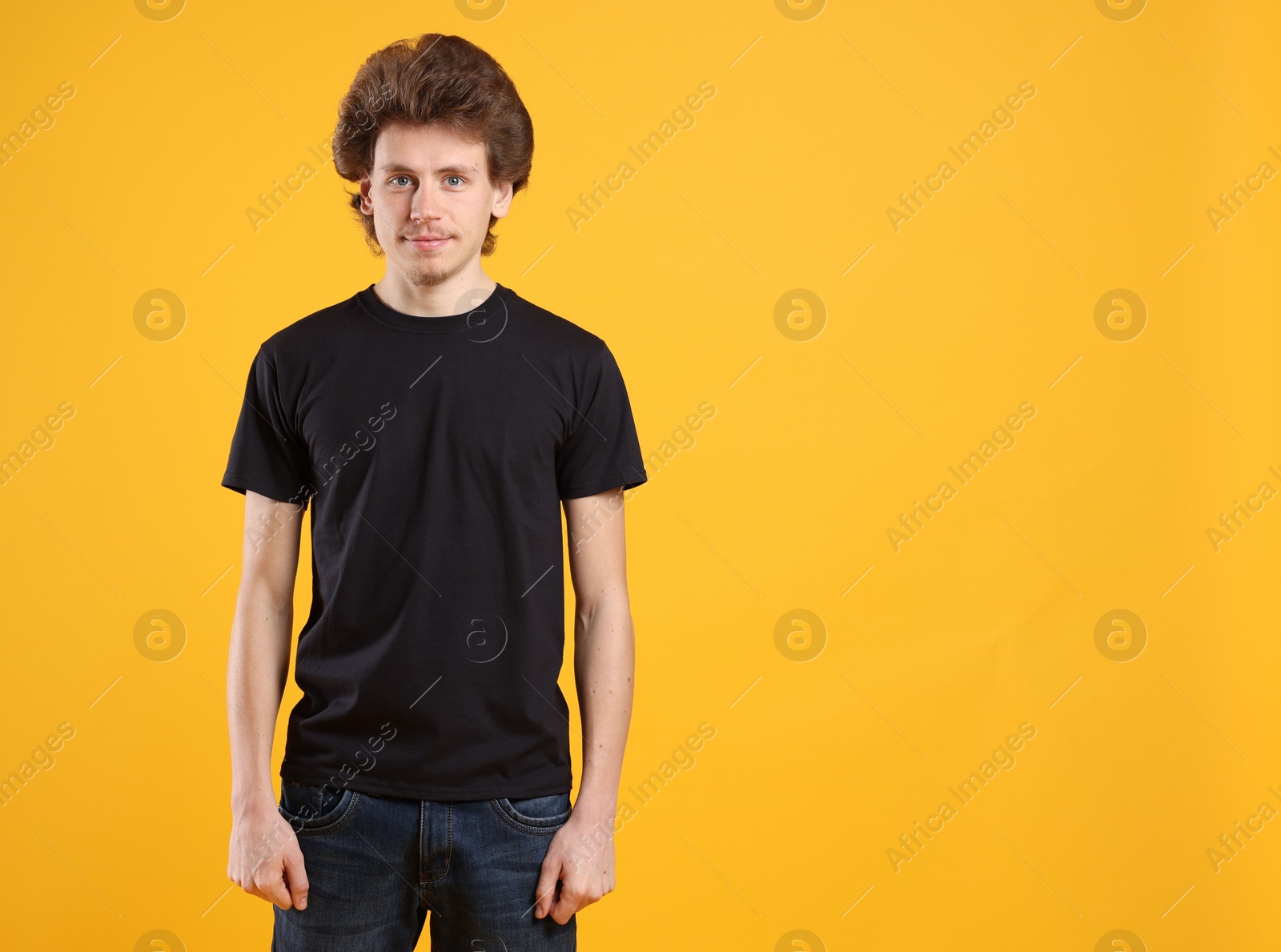 Photo of Young man wearing blank black t-shirt on orange background. Mockup for design