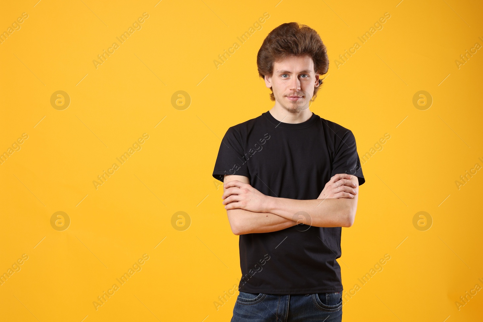 Photo of Young man wearing blank black t-shirt on orange background. Mockup for design