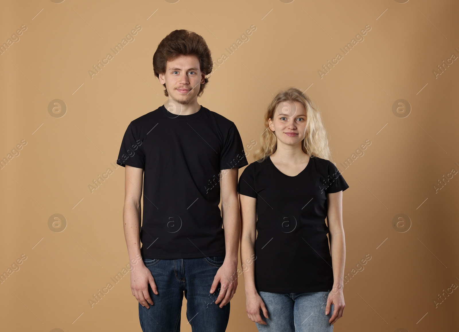 Photo of Young woman and man wearing blank black t-shirts on light brown background. Mockup for design