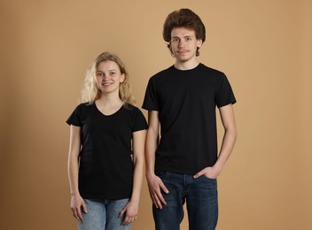 Photo of Young woman and man wearing blank black t-shirts on light brown background. Mockup for design