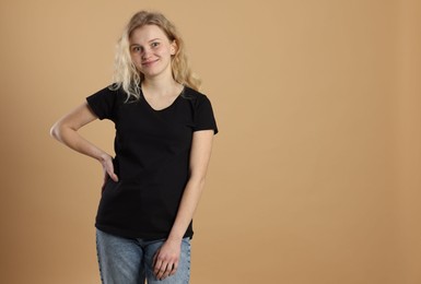 Photo of Young woman wearing blank black t-shirt on light brown background. Mockup for design