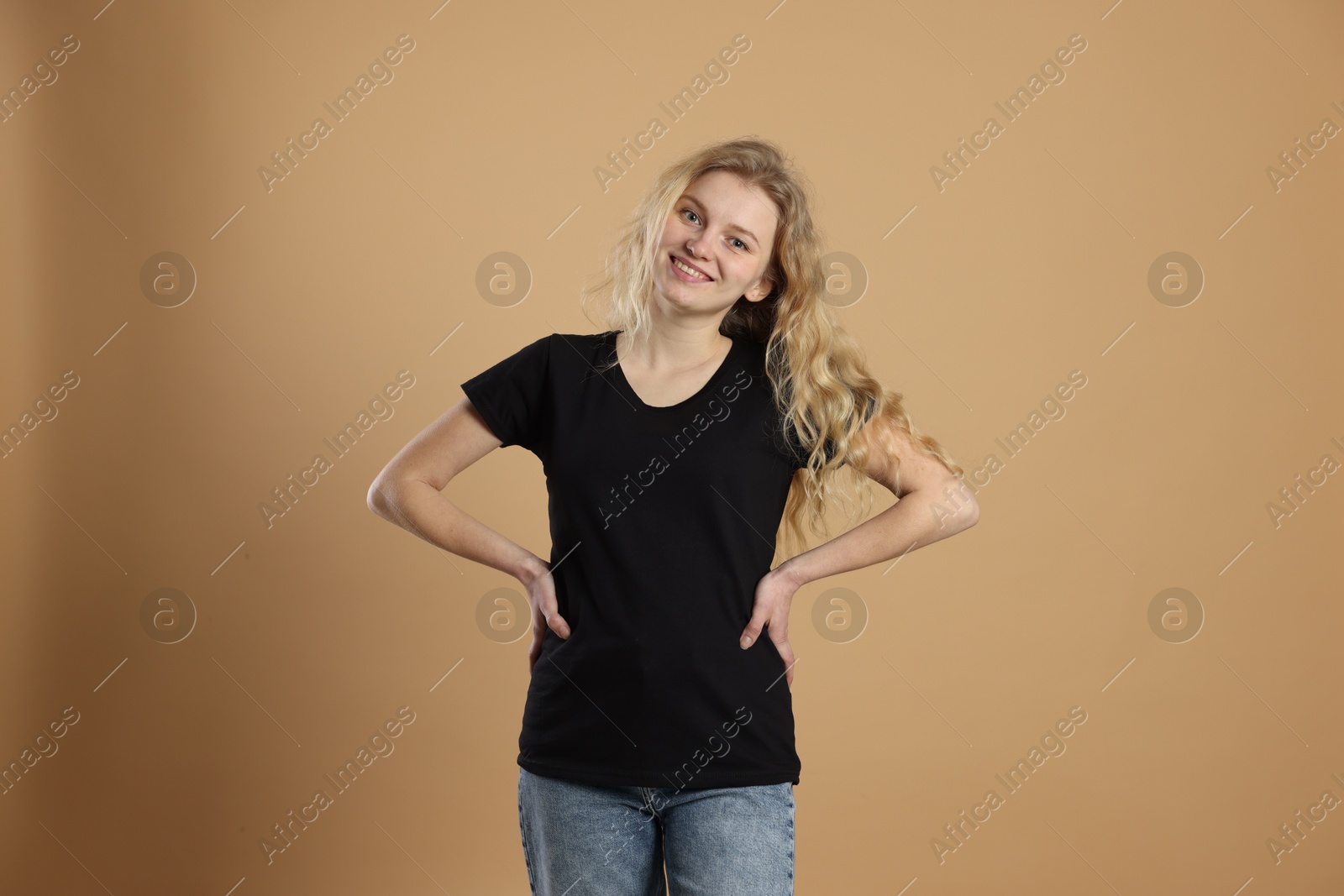 Photo of Young woman wearing blank black t-shirt on light brown background. Mockup for design