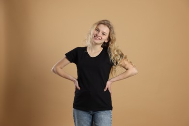 Photo of Young woman wearing blank black t-shirt on light brown background. Mockup for design