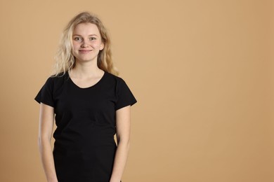 Photo of Young woman wearing blank black t-shirt on light brown background. Mockup for design