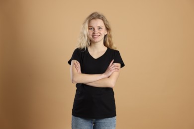 Photo of Young woman wearing blank black t-shirt on light brown background. Mockup for design