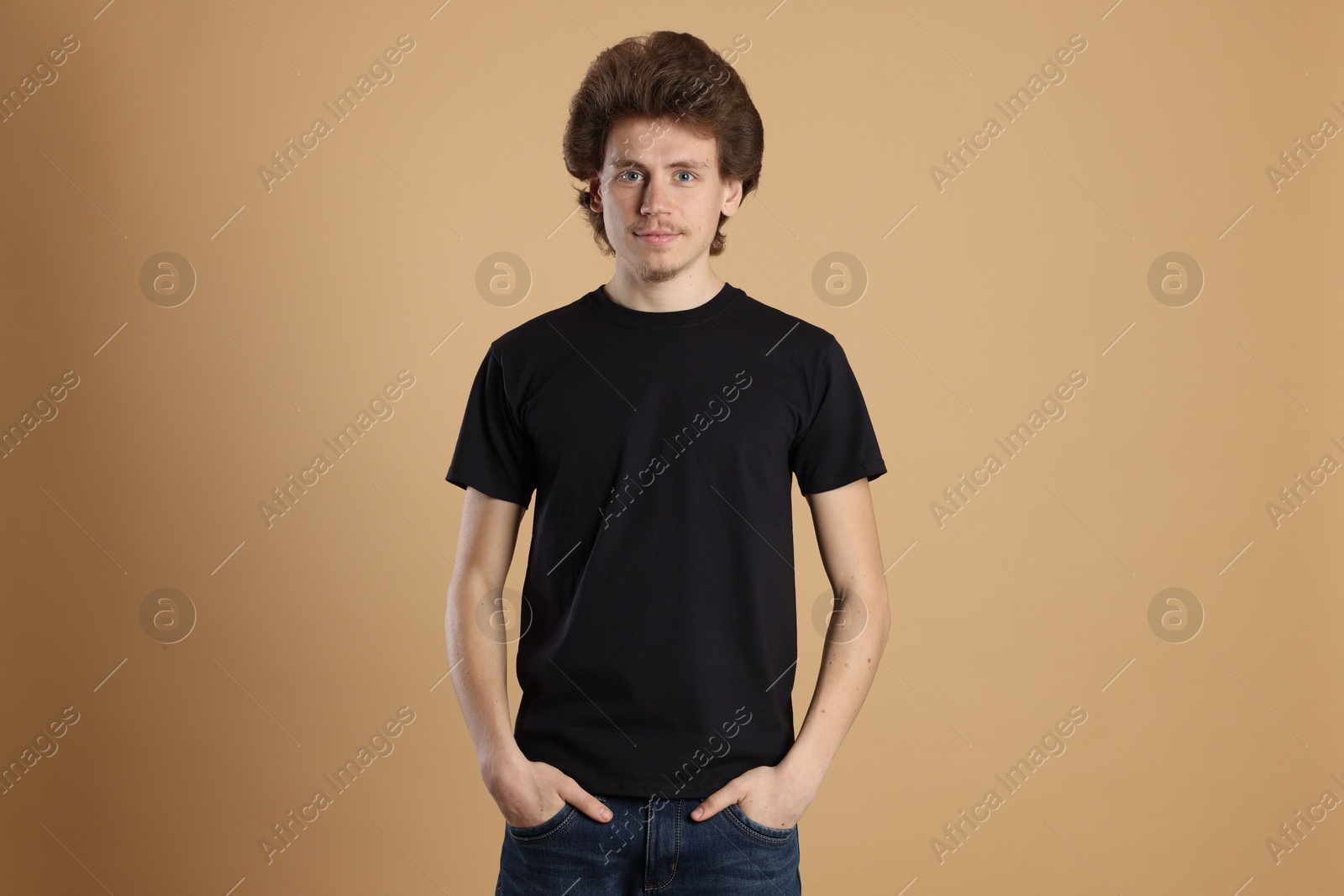 Photo of Young man wearing blank black t-shirt on light brown background. Mockup for design