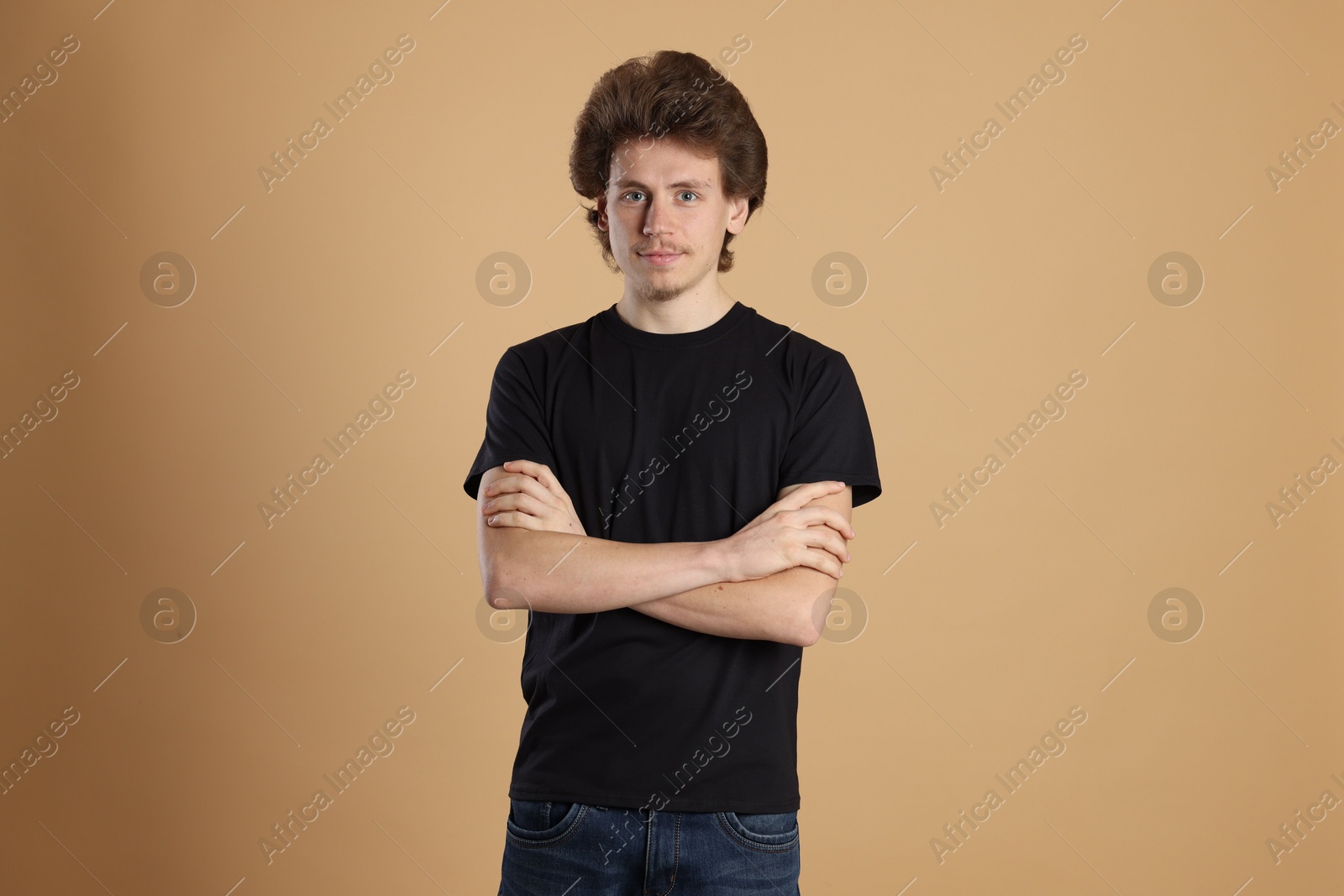 Photo of Young man wearing blank black t-shirt on light brown background. Mockup for design