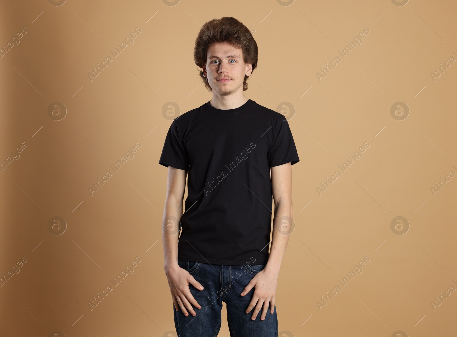 Photo of Young man wearing blank black t-shirt on light brown background. Mockup for design