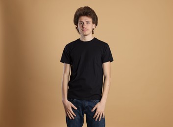 Photo of Young man wearing blank black t-shirt on light brown background. Mockup for design