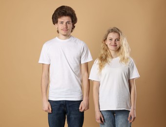 Photo of Young woman and man wearing blank white t-shirts on light brown background. Mockup for design