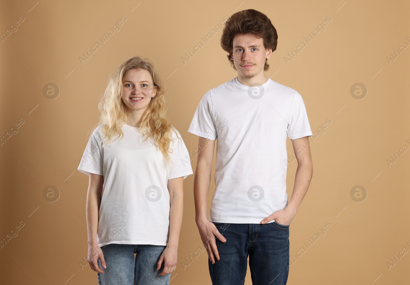 Photo of Young woman and man wearing blank white t-shirts on light brown background. Mockup for design