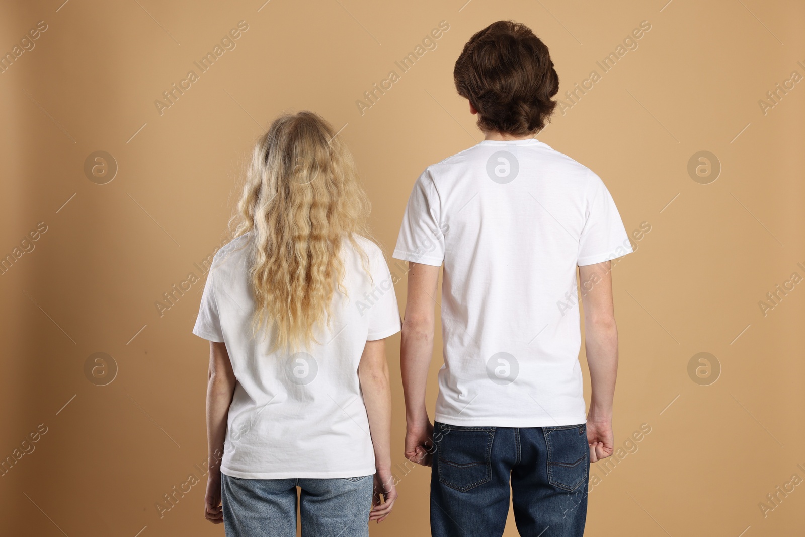 Photo of Young woman and man wearing blank white t-shirts on light brown background, back view. Mockup for design