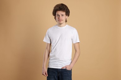 Photo of Young man wearing blank white t-shirt on light brown background. Mockup for design