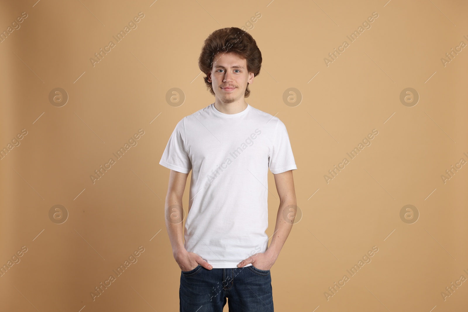 Photo of Young man wearing blank white t-shirt on light brown background. Mockup for design