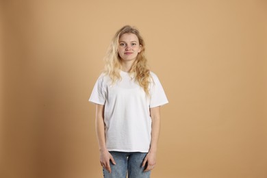 Photo of Young woman wearing blank white t-shirt on light brown background. Mockup for design