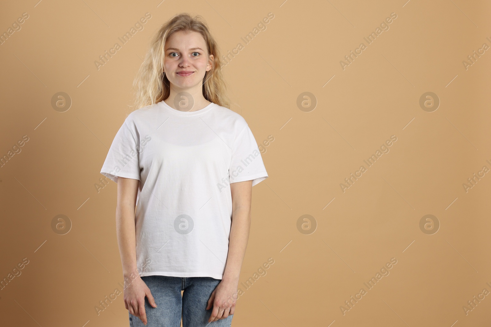 Photo of Young woman wearing blank white t-shirt on light brown background. Mockup for design