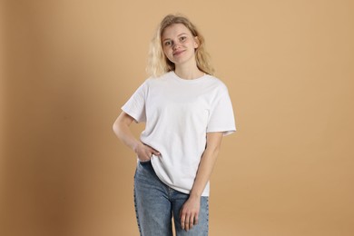 Photo of Young woman wearing blank white t-shirt on light brown background. Mockup for design