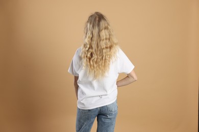 Photo of Young woman wearing blank white t-shirt on light brown background, back view. Mockup for design