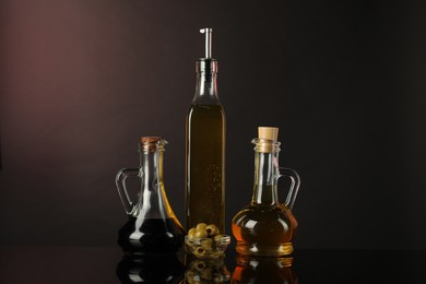 Photo of Salad dressings and olives on mirror surface against dark background