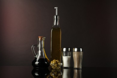 Photo of Salad dressings, spices and olives on mirror surface against dark background