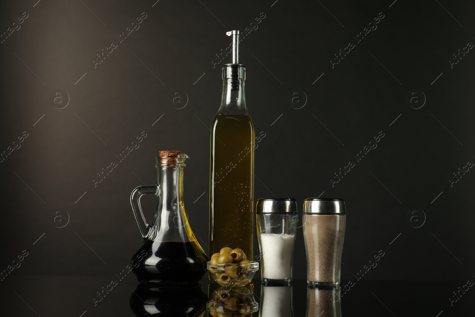 Photo of Salad dressings, spices and olives on mirror surface against black background