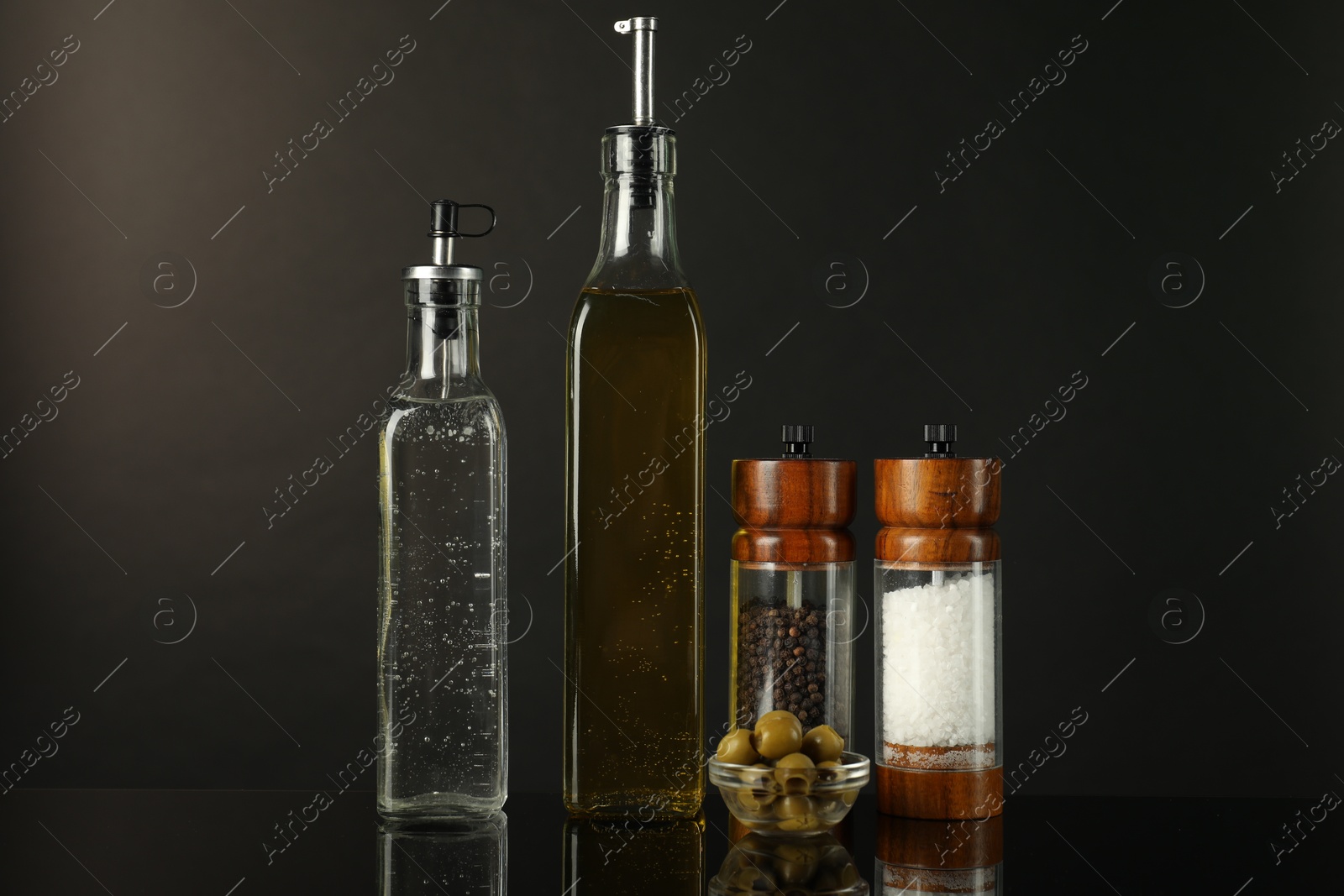 Photo of Salad dressings, spices and olives on mirror surface against black background