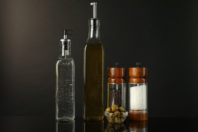 Photo of Salad dressings, spices and olives on mirror surface against black background