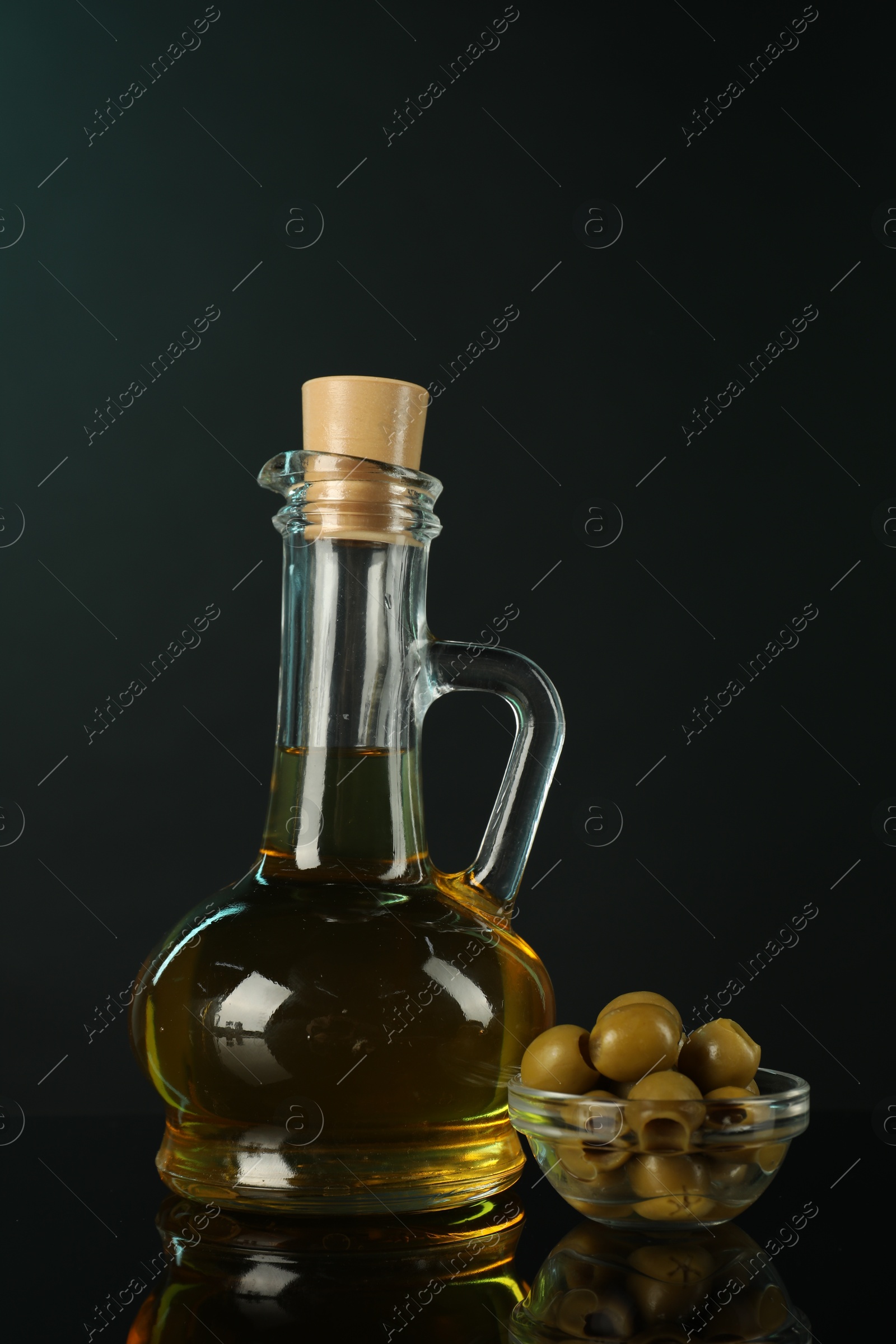 Photo of Oil in bottle and olives on mirror surface against black background