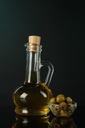 Photo of Oil in bottle and olives on mirror surface against black background