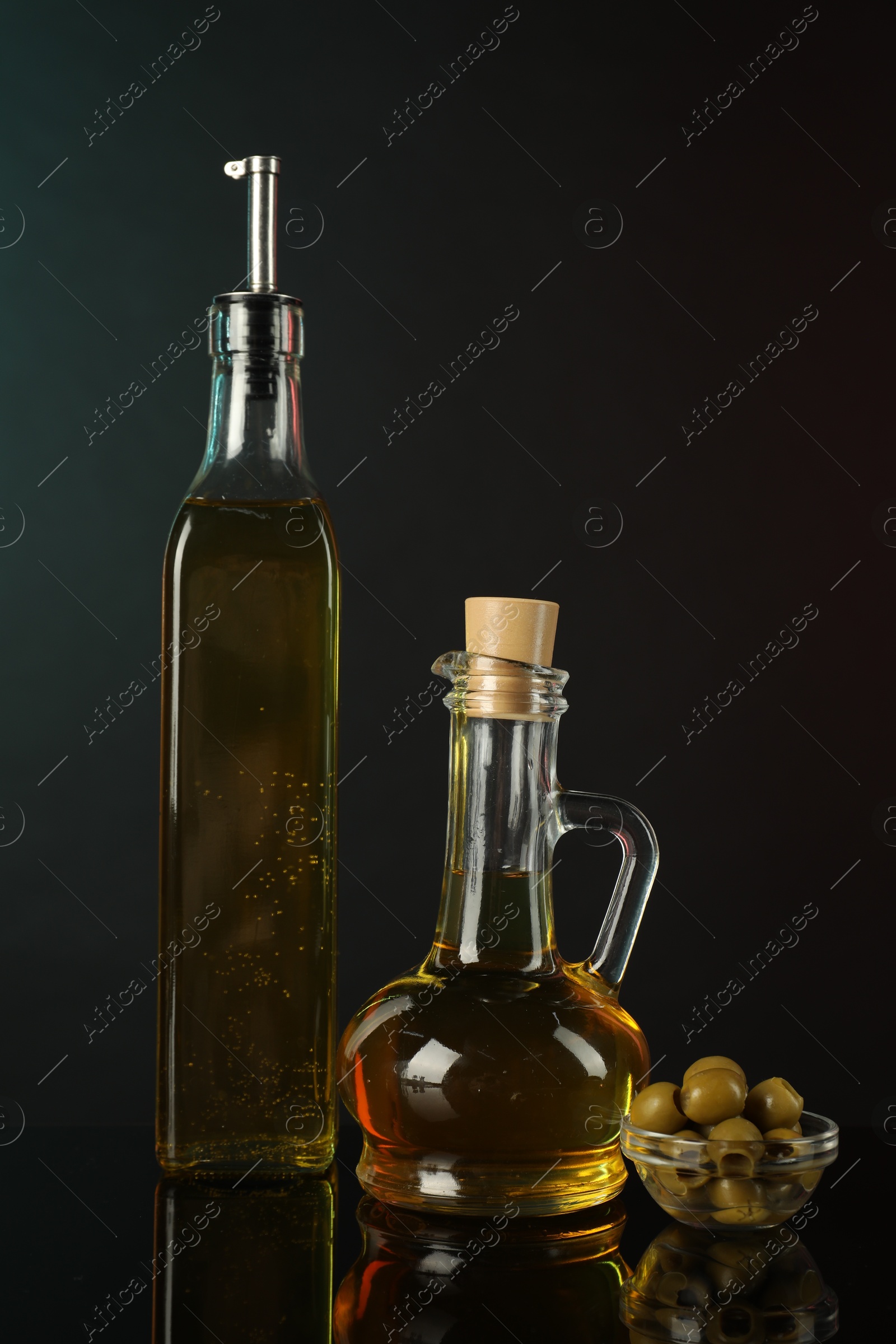 Photo of Oils in bottles and olives on mirror surface against dark background