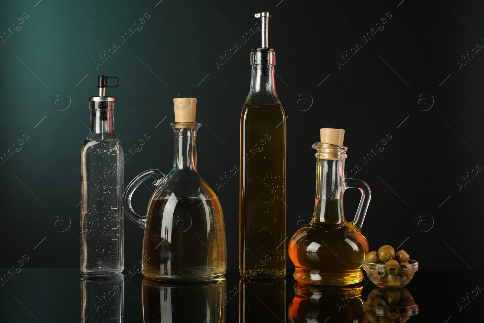 Photo of Salad dressings and olives on mirror surface against black background