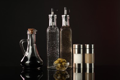 Photo of Salad dressings, spices and olives on mirror surface against dark background