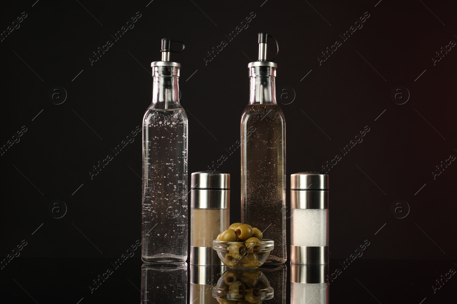 Photo of Salad dressings, spices and olives on mirror surface against dark background