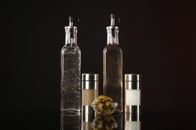 Photo of Salad dressings, spices and olives on mirror surface against dark background