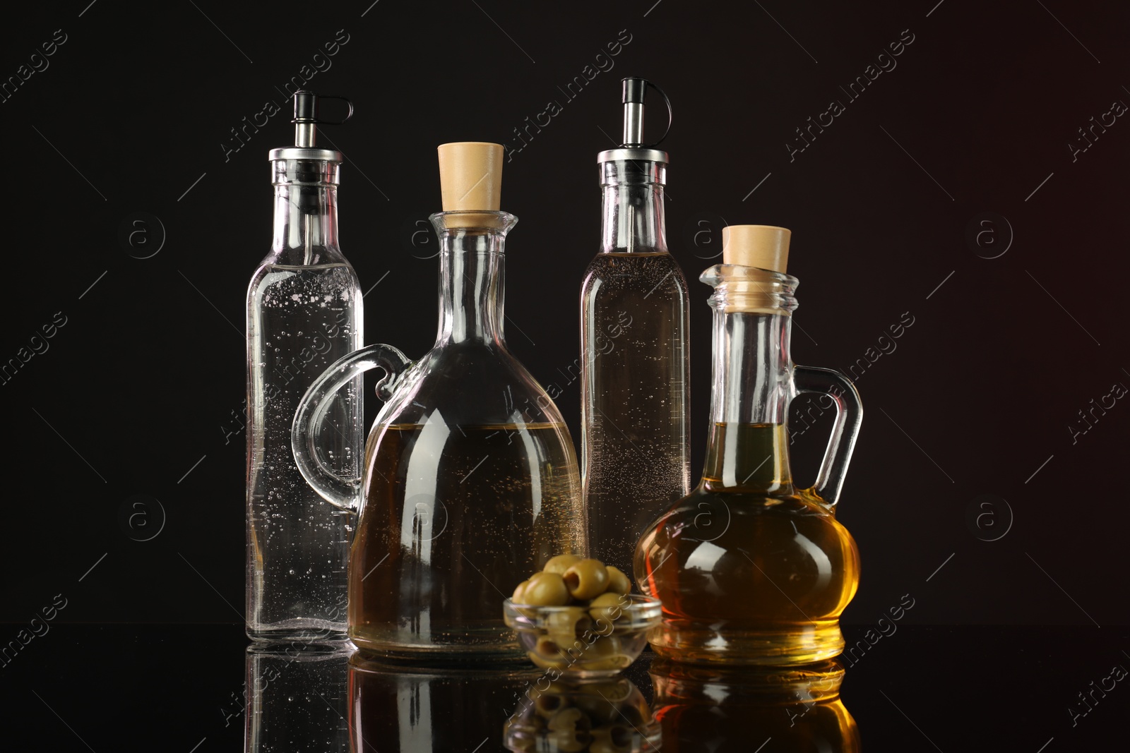 Photo of Salad dressings and olives on mirror surface against dark background