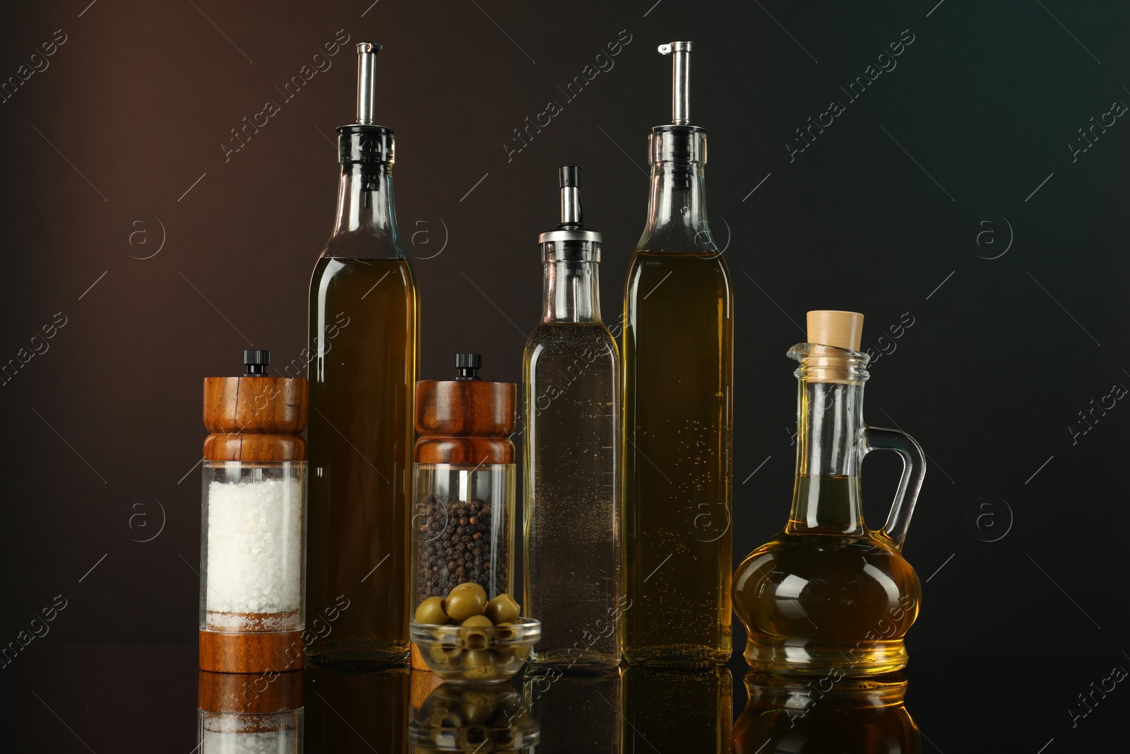 Photo of Salad dressings, spices and olives on mirror surface against dark background