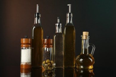 Photo of Salad dressings, spices and olives on mirror surface against dark background