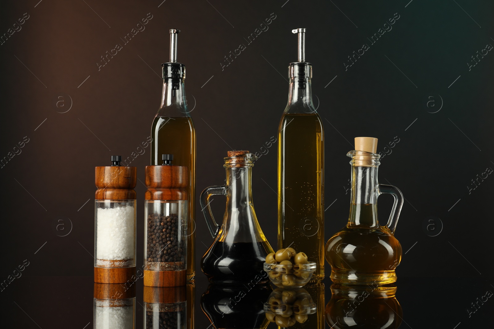 Photo of Salad dressings, spices and olives on mirror surface against dark background