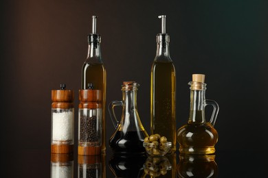 Photo of Salad dressings, spices and olives on mirror surface against dark background