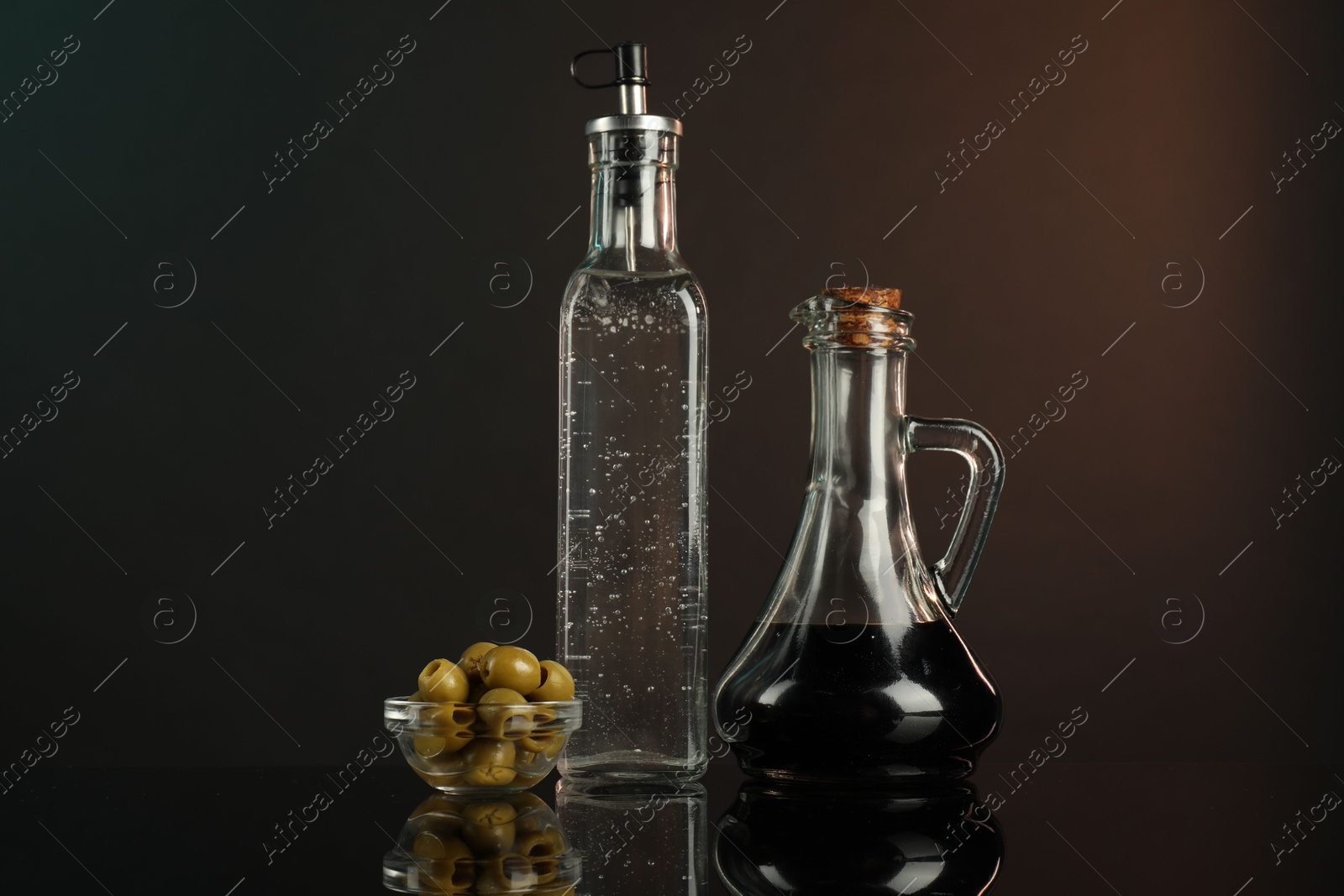 Photo of Salad dressings and olives on mirror surface against dark background