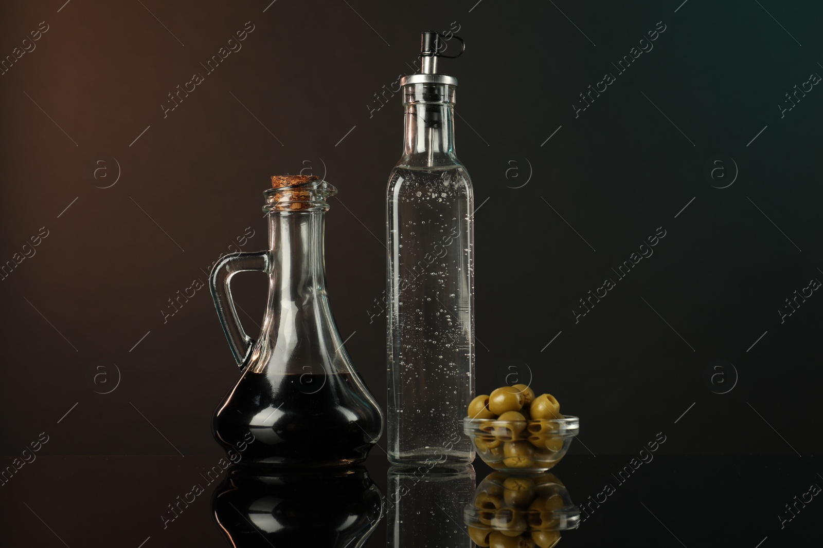 Photo of Salad dressings and olives on mirror surface against dark background