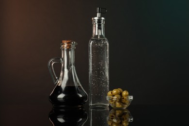 Photo of Salad dressings and olives on mirror surface against dark background