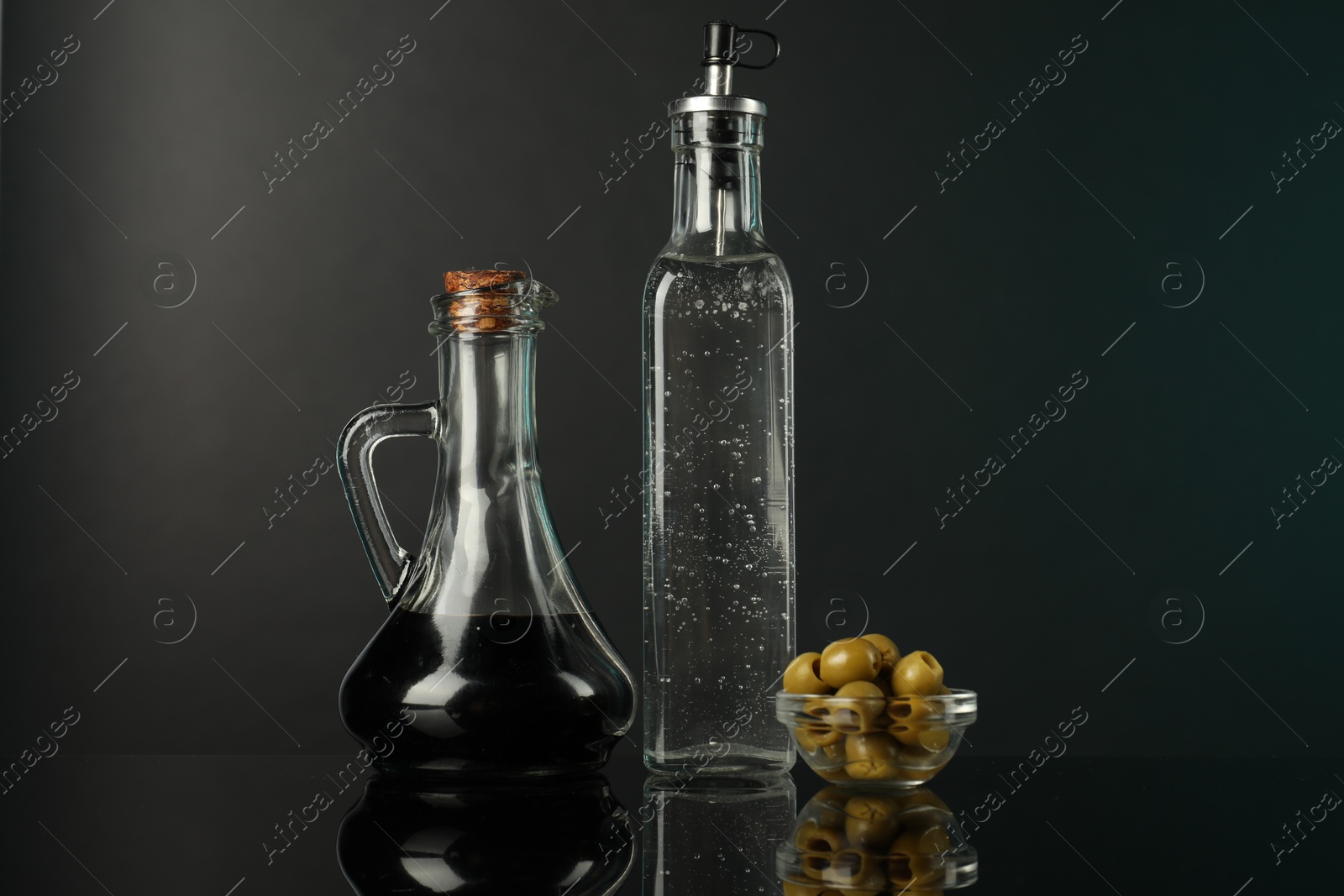 Photo of Salad dressings and olives on mirror surface against black background