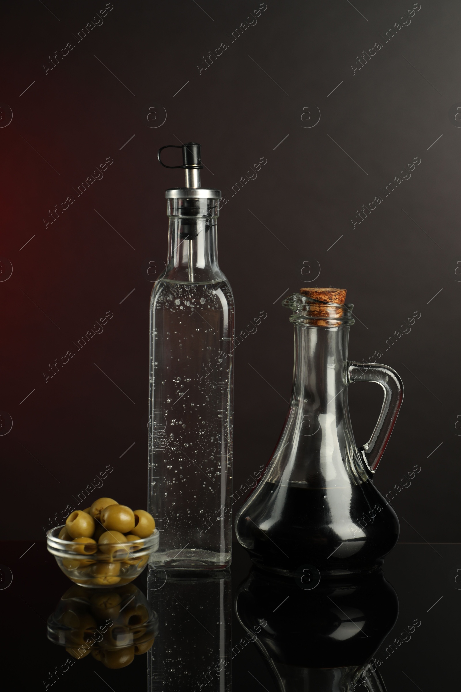 Photo of Salad dressings and olives on mirror surface against dark background